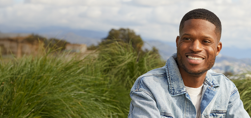 جاستن يبتسم وهو جالس في ساحة بالهواء الطلق، وفي الخلفية السماء والأشجار.