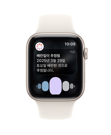 건강 앱의 생리 주기 추적에서 배란 추정일 알림이 표시되고 Digital Crown이 보이는 스타라이트 색상 알루미늄 케이스의 Apple Watch SE 3, 그리고 스타라이트 색상 스포츠 밴드