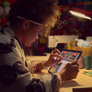 Eine Person sitzt an einem Arbeitstisch und zoomt mit zwei Fingern auf einem iPad Display ein Bild ein.