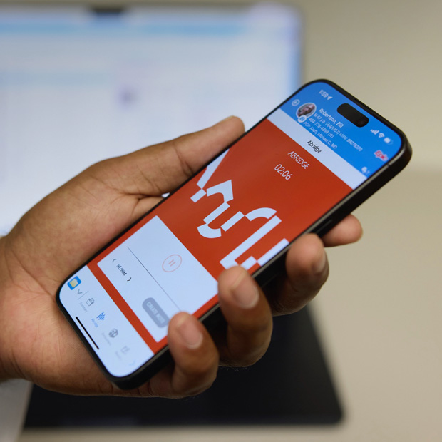 Uma mão segura um iPhone com o app Abridge aberto, que transforma conversas entre profissionais de saúde e pacientes em notas clínicas organizadas.