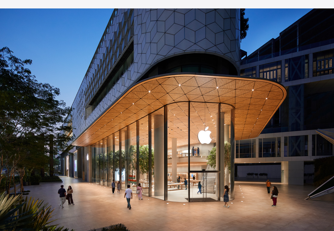 Apple Store noću, stakleni prozori, osvijetljeno iznutra, Apple logo u sredini iznad glavnih vrata.