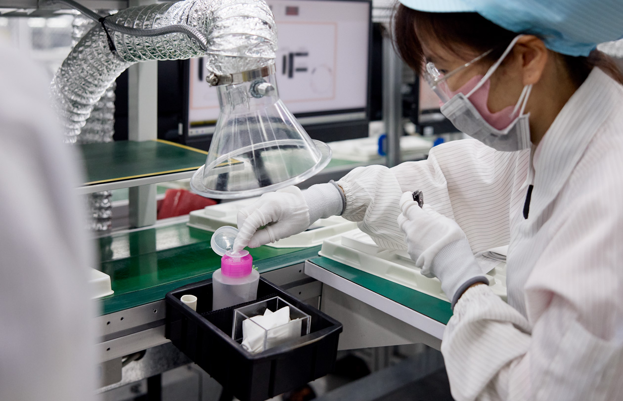 An employee in full safety uniform works at a station at an Apple Watch assembly facility
